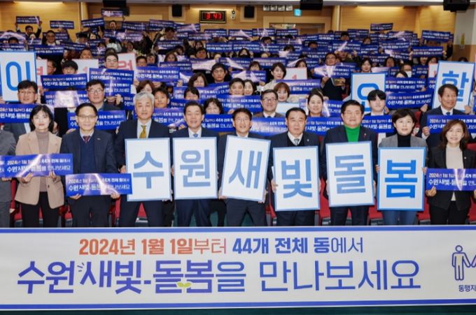 <strong>지난해 12월 수원시 관계자들이 수원새빛돌봄 전체 동 확대를 홍보하는 손팻말을 들어 보이고 있다.</strong>